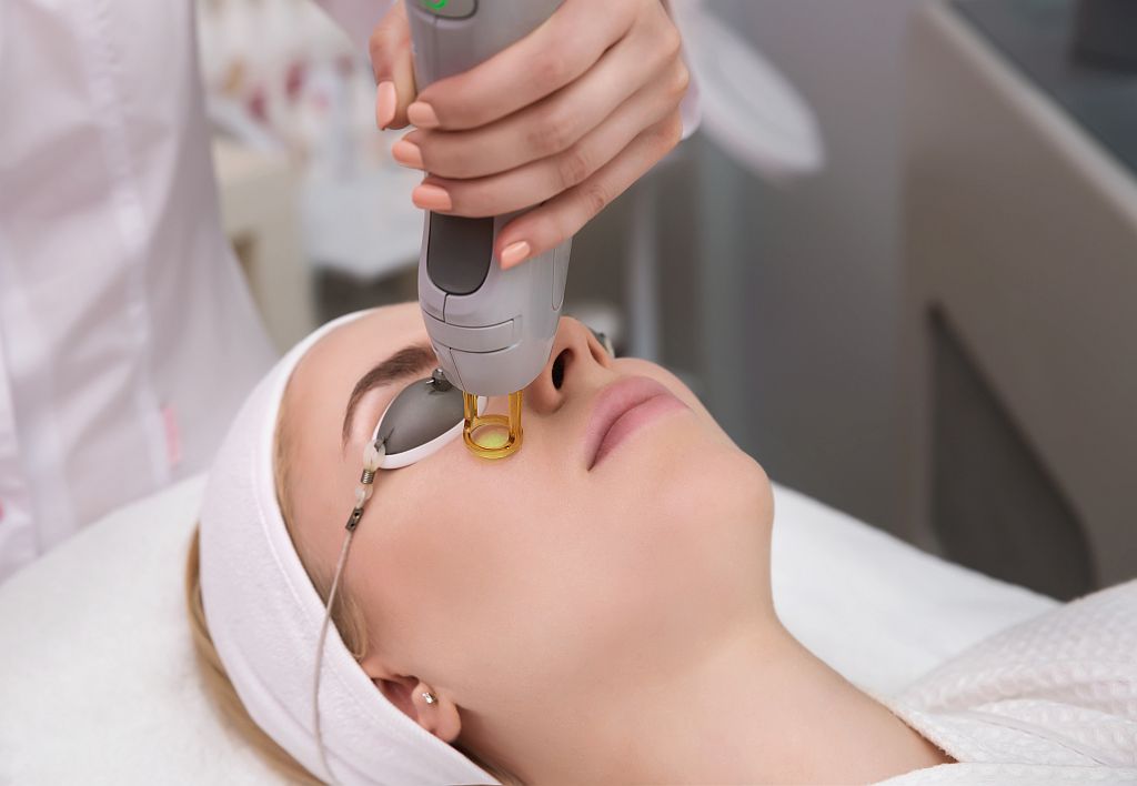 Therapist beautician makes a laser treatment to young woman's fa